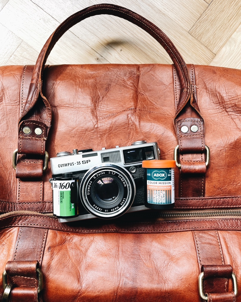 Olympus 35SP mit analogen Filmen liegt auf einer Reisetasche